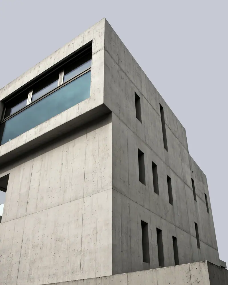Edifício residencial de concreto aparente com janelas estreitas e uma longa janela horizontal no último pavimento, contra o céu.