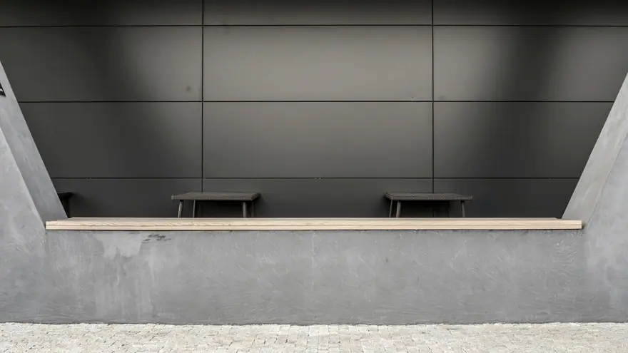 Parede de concreto com recorte horizontal que forma um banco contínuo com assento de madeira.
