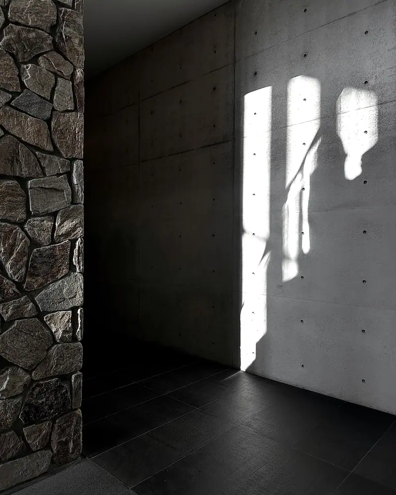 Parede de pedra ao lado de uma parede de concreto iluminada por feixes de sol.